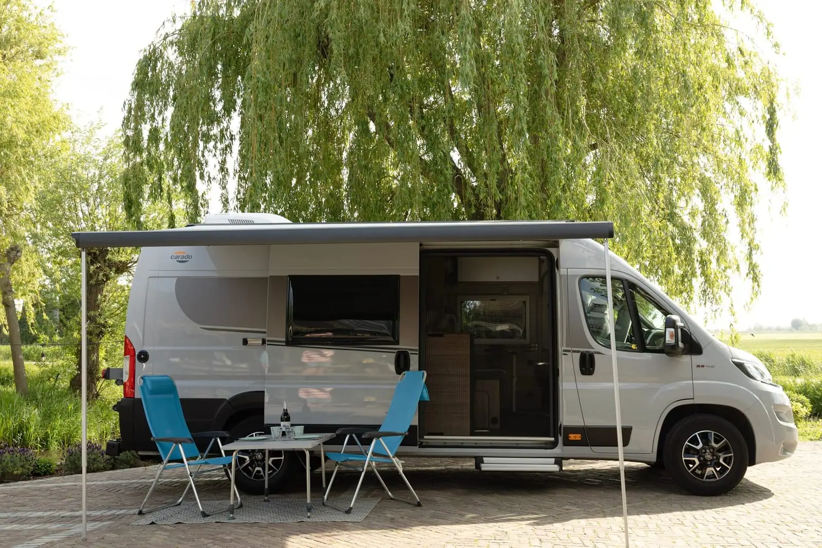 Carado CVE 640 van opzij met uitgedraaide luifel, open schuifdeur en twee stoelen