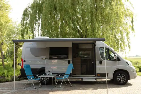 Carado CVE 640 van opzij met uitgedraaide luifel, open schuifdeur en twee stoelen