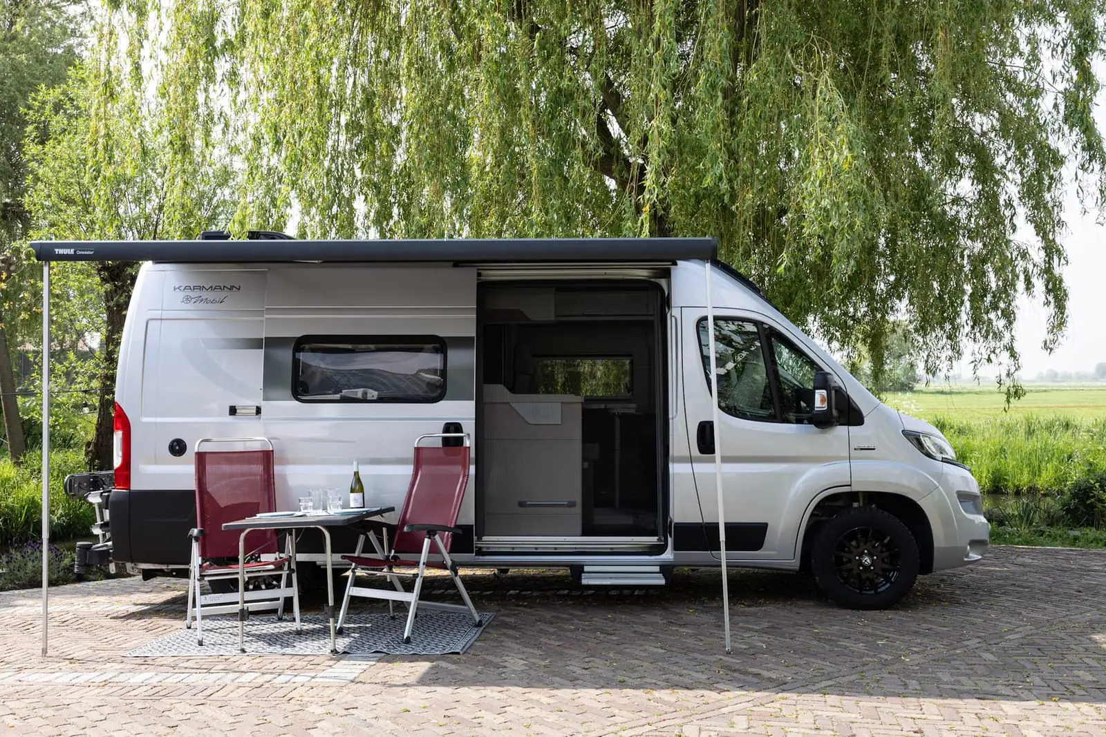 Karmann Mobil Davis Lifestyle 600 van opzij met luifel, open schuifdeur en stoelen