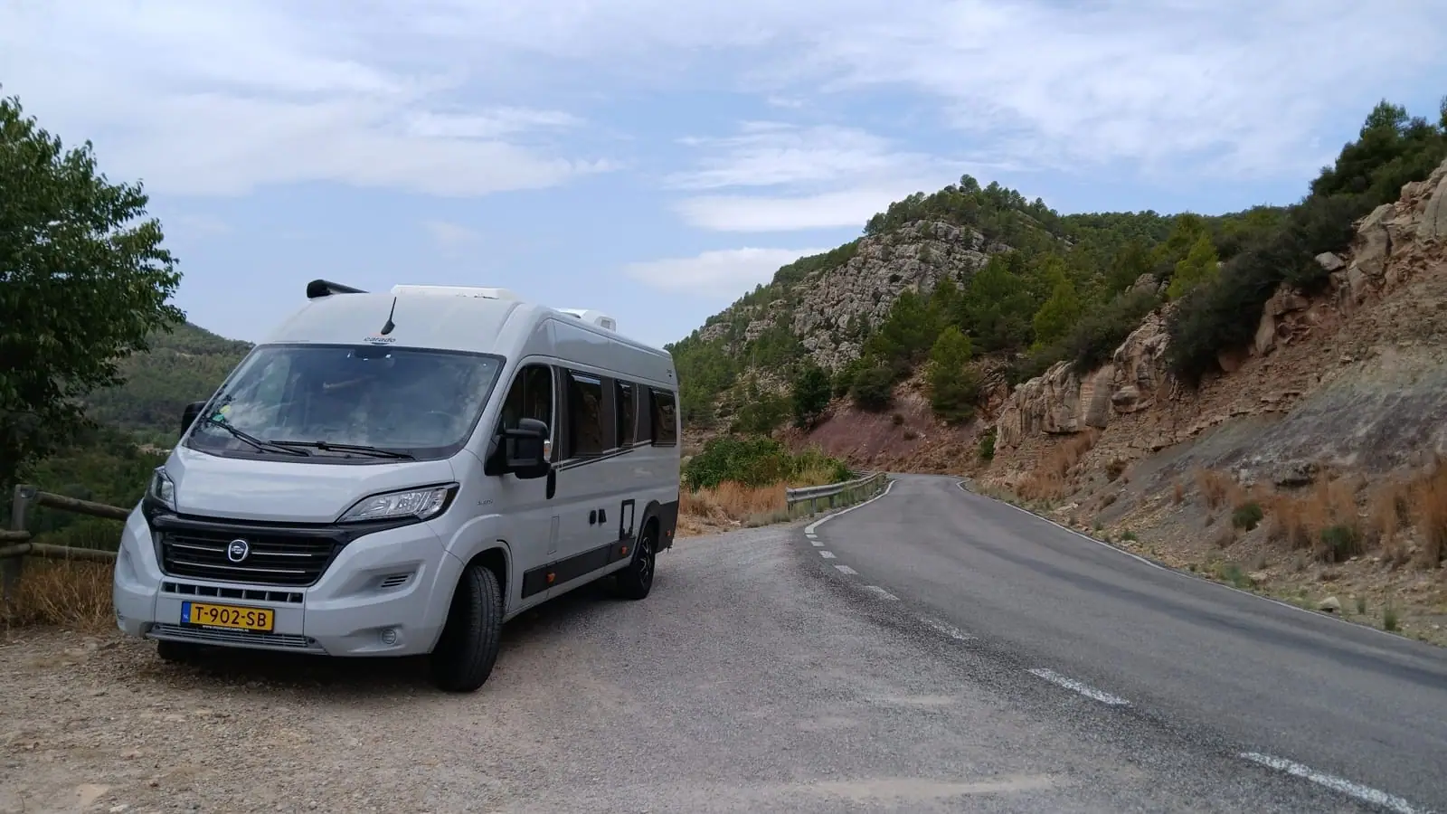 De camper op een bergweg in Spanje, met rotswanden en dennenbomen langs de weg
